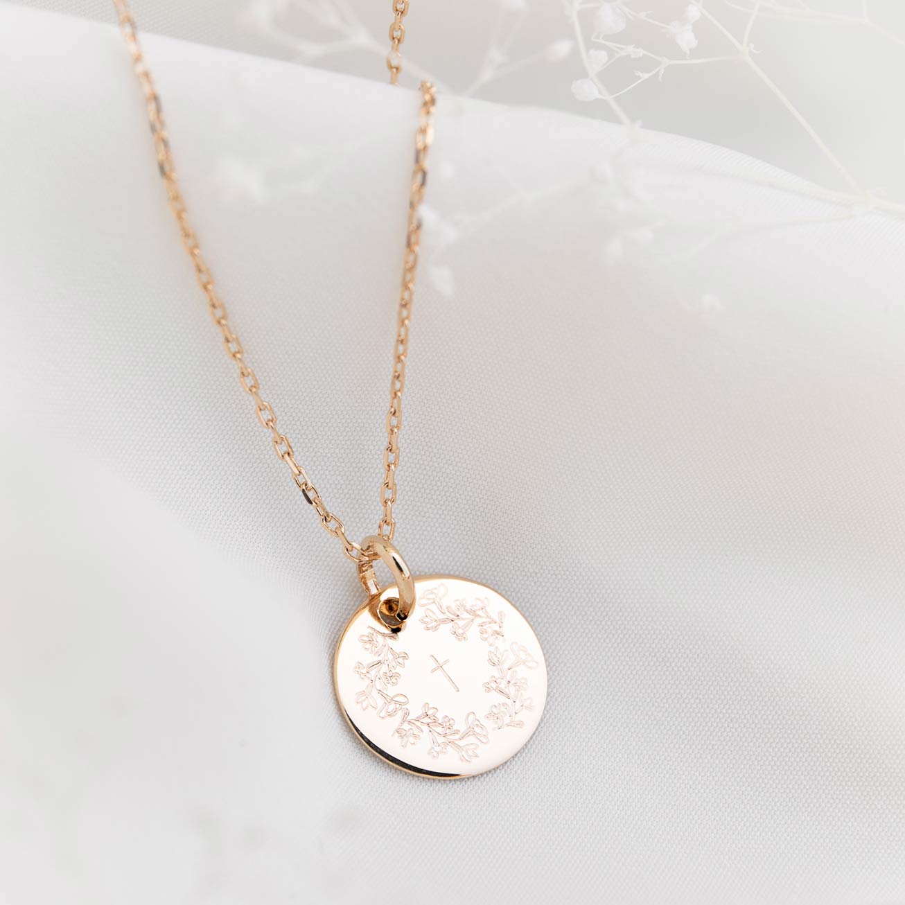 Christening medal featuring a wreath of flowers an