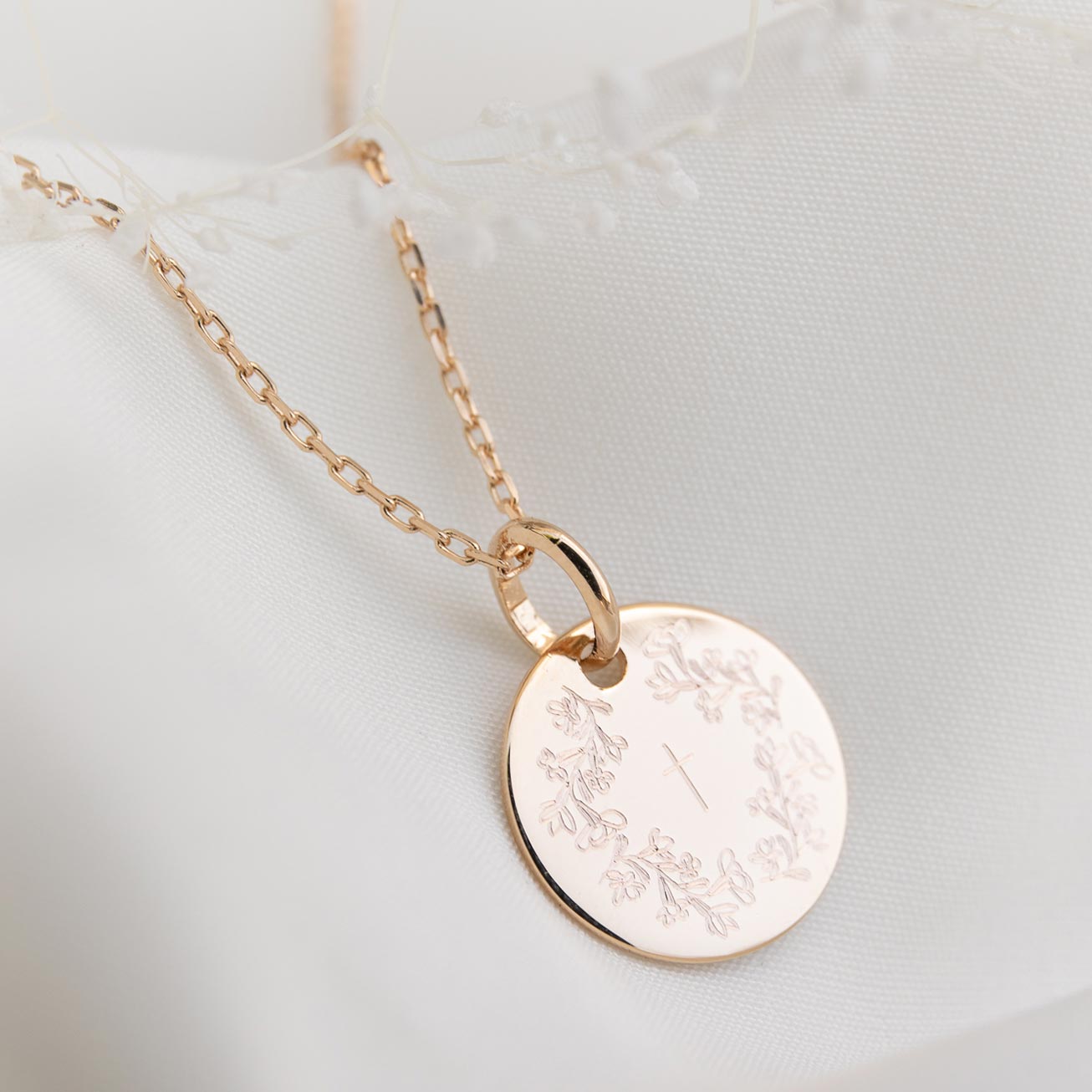 Christening medal featuring a wreath of flowers an