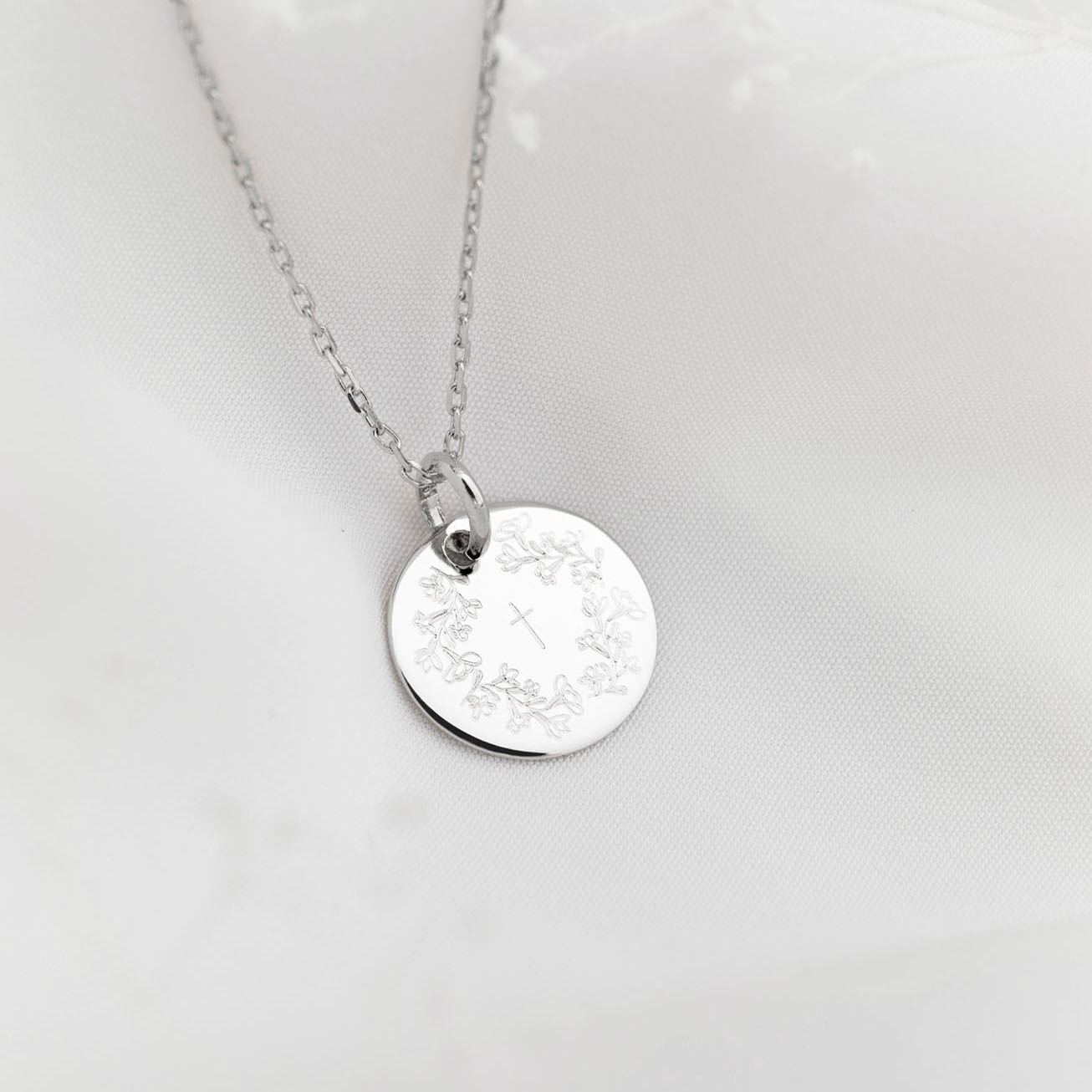 Silver baptismal medal with a wreath of flowers an